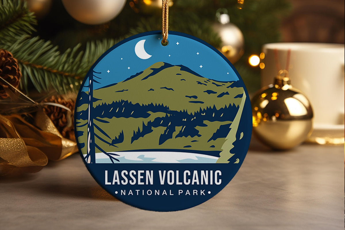A round, stylized ornament depicting the majestic landscape of Lassen Volcanic National Park. The design features a layered composition of dark, rugged mountain ranges silhouetted against a deep blue night sky doTed with stars and a crescent moon. In the foreground, a body of water reflects the cool tones of the scene. The inscription "LASSEN VOLCANIC NATIONAL PARK" anchors the view, celebrating the dramatic, serene beauty of the volcanic wilderness. 
