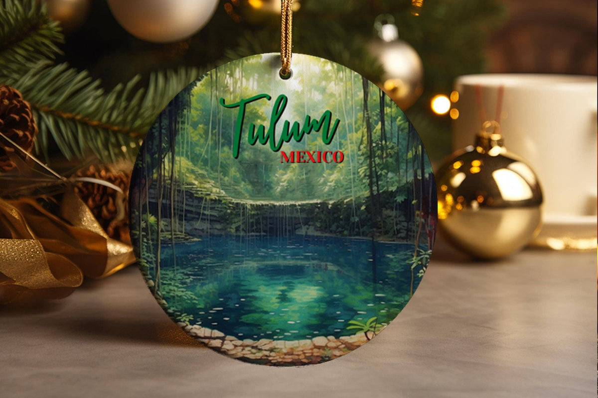 The ornament captures a tranquil and mystical scene from a cenote in Tulum, Mexico. The illustration is dominated by the deep, cool tones of the water, rendered in various shades of emerald and deep blue, suggesting the crystal clarity and depth of the cenote pool. Surrounding the pool, the scene is framed by lush, dark green foliage and tall trees, creating a sense of enclosure and tranquility. The scene is minimal yet powerful, with the word "TULUM" clearly displayed above the body of water, and "MEXICO" 