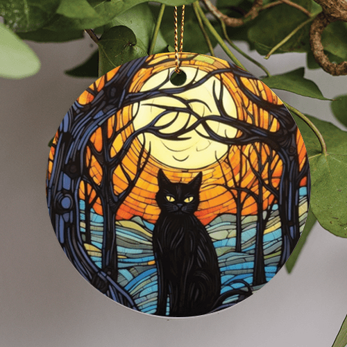 This halloween holiday ornament is in an art style like stained colored glass presenting the appearance of light passing through. This ornamental and pictorial image is of a traditional black cat, with yellow eyes sitting in the middle of some bare woodland trees. A harvest moon sits in an orange nights sky.