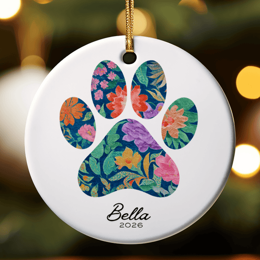 Decorative ornament with floral paw print design and 'Bella 2026' text on a blurred background.