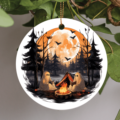 This halloween holiday ornament is in a whimsical pulp art style of two happy sheeted ghosts. Reading among the camp fire light in the woods surrounded by gray pine trees tiny pumpkins and bats. Bats in the sky flying in front of a full harvest moon.