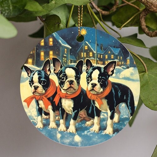 This holiday ornament displays three Boston Terrier puppies with red scarves standing on an icy patch with a snowy town behind during a blue evening in a Rockwell inspired painting style.