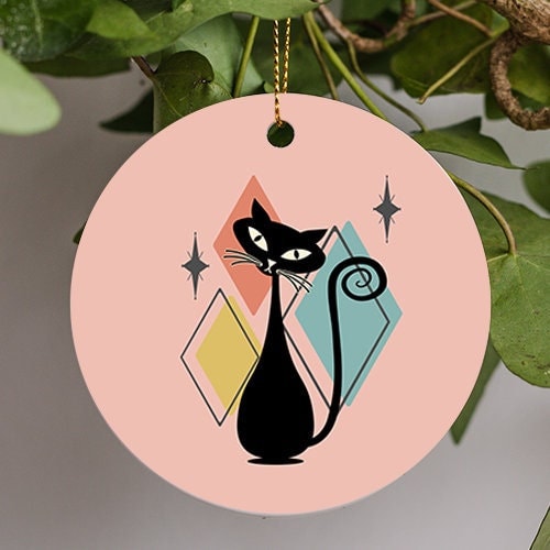 This holiday ornament shows a Mid-Century Cat with a pink retro mid-twentieth century jazzy background and atomic stars. A slender silhouetted cats leans his happy head to the side in front.