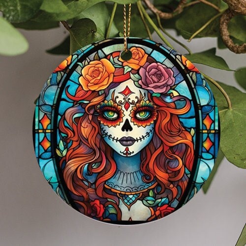 his holiday ornament is for The Day of the Dead Celebration. A stained glass design decorates the background. A long red haired sugar skull woman with flowers sits in front.