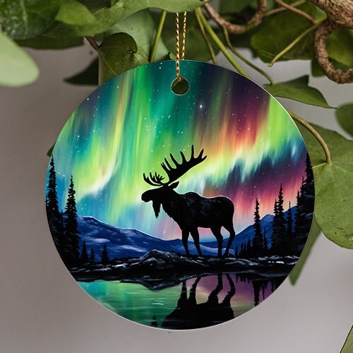 This holiday ornament shows the colorful Northern Lights. Pine trees scattered off to the sides. A frozen reflective lake sits in the middle as a giant Moose admires the nights starry colorful sky.