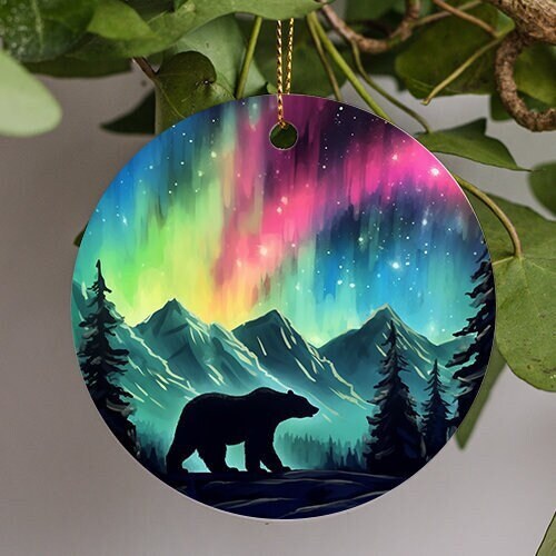 This holiday ornament shows the colorful Northern Lights. Pine trees scattered off to the sides. A Bear walks by and admires the nights starry colorful sky.