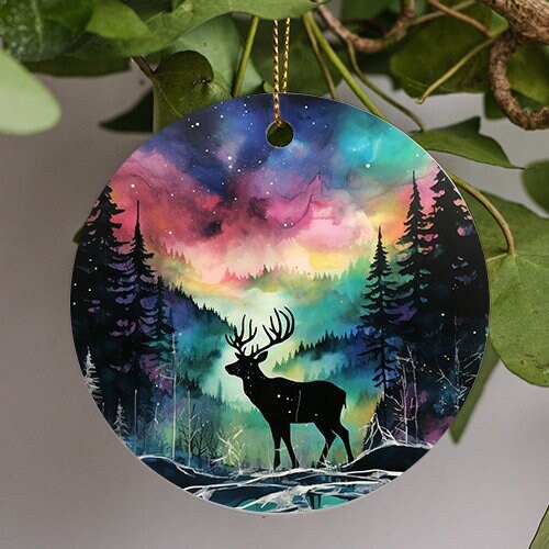 This holiday ornament shows the colorful Northern Lights. Pine trees scattered off to the sides. A snow mound sits in the middle with a great Buck admires the nights starry colorful sky.