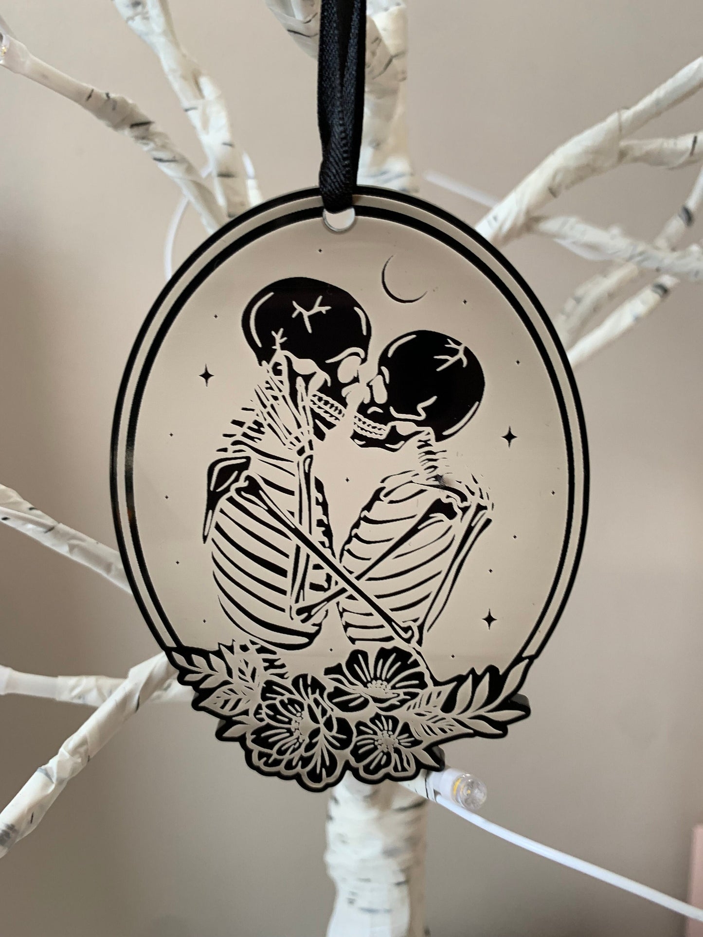 This holiday ornament shows two skeleton crossed lovers under a crescent moon starry sky, in an oval frame and flowers toward the bottom.