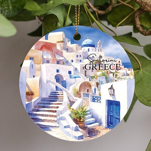 This holiday ornament shows Santorini Greece. With it whitewashed edifices, candy colored houses, paved pathways and blue domes surrounded by a warm blue colored clouded sky and ocean background.