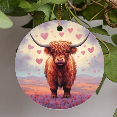 This ornament is of a loving baby highland cow standing in warm sand colored valley with the floor lined with fire red flower and soft shaped loving heart clouds float around the happy little cow.