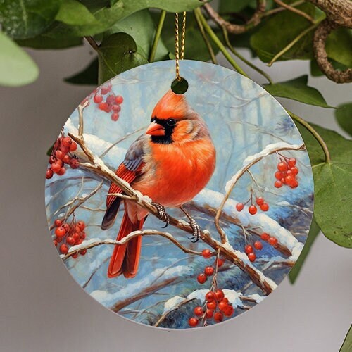 This ornament depicts a snowy wintery scene of a Northern Cardinal. The soft red plumage plump like a small tomato. Its head tilted away from the wild berries situated around this little friend perched on a branch this chilly winter morning.