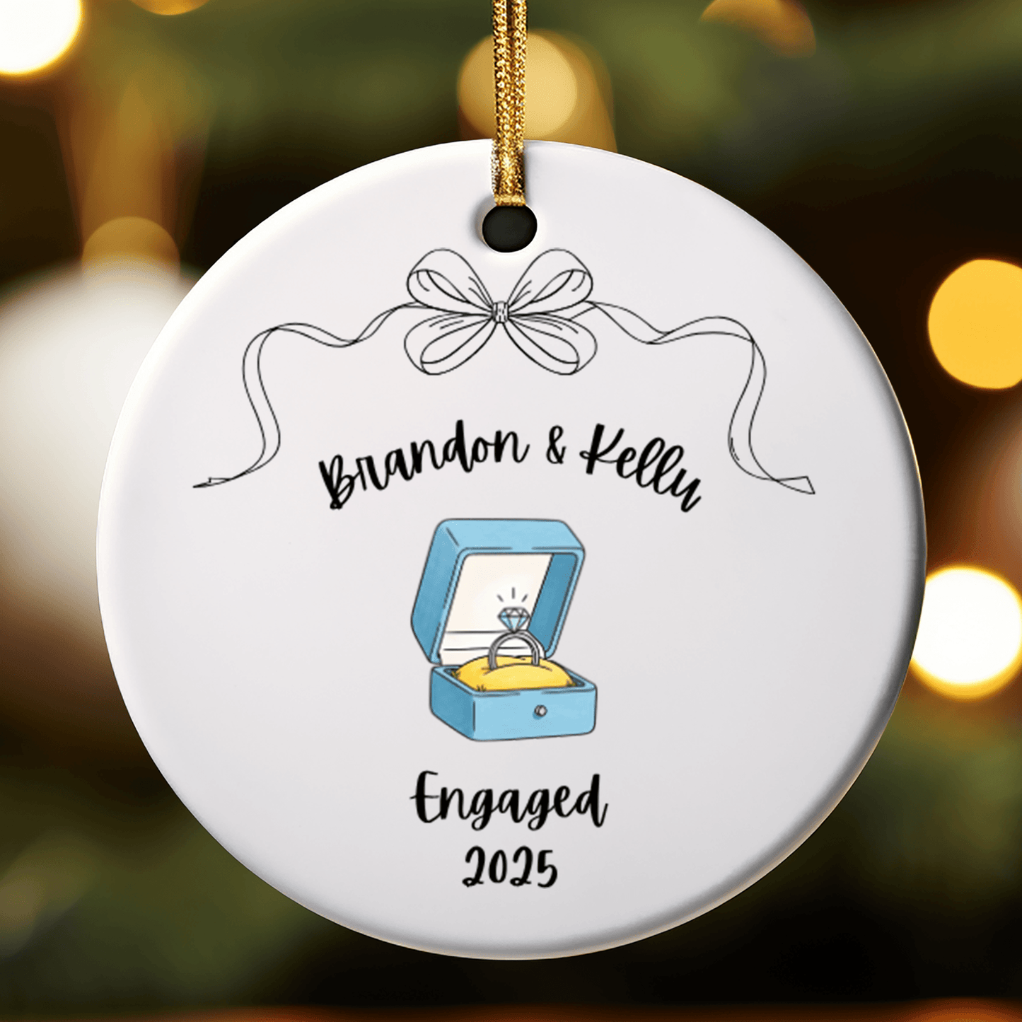 Round ornament with 'Brandon & Kelly' and 'Engaged 2025' text, featuring a ring box illustration on a blurred lights background.